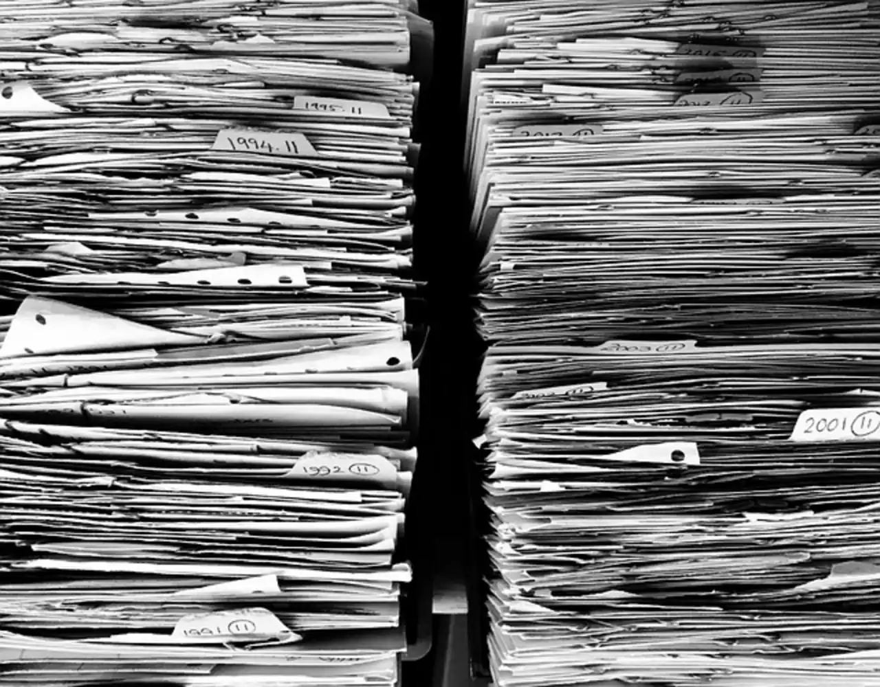 Two stacks of paper files piled on shelves, in black and white
