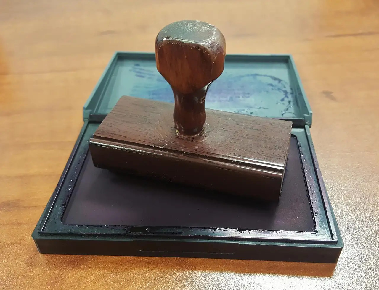 A wooden rubber stamp resting on an open ink pad on a desk.